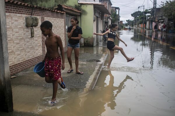 Jóvenes caminando por una calle inundada tras las fuertes lluvias en Duque de Caxias, Brasil.Las intensas lluvias de la semana pasada en Brasil causaron varios muertos. - Sputnik Mundo