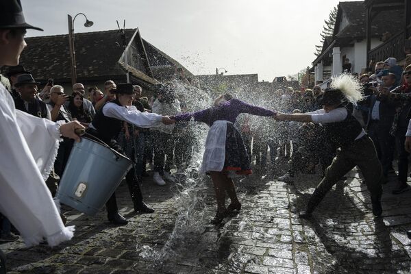 Hombres húngaros vestidos con trajes típicos vierten agua sobre las mujeres durante una celebración tradicional del Lunes de Pascua en Holloko, Hungría. Este ritual de Pascua es común principalmente en Europa central. - Sputnik Mundo