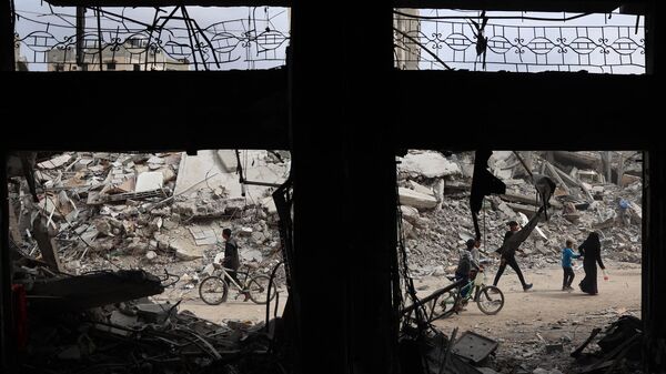 Palestinos pasan junto a edificios destruidos por Israel en Jan Yunis el 8 de abril de 2024, después de que Tel Aviv retirara a sus fuerzas terrestres del sur de la Franja de Gaza - Sputnik Mundo