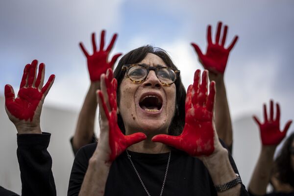 Familiares y activistas de los rehenes retenidos en la Franja de Gaza gritan y levantan las manos pintadas de rojo, en Israel. - Sputnik Mundo