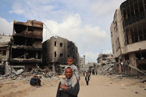 Palestinos pasan cerca de edificios destruidos en Khan Younis, Palestina. - Sputnik Mundo