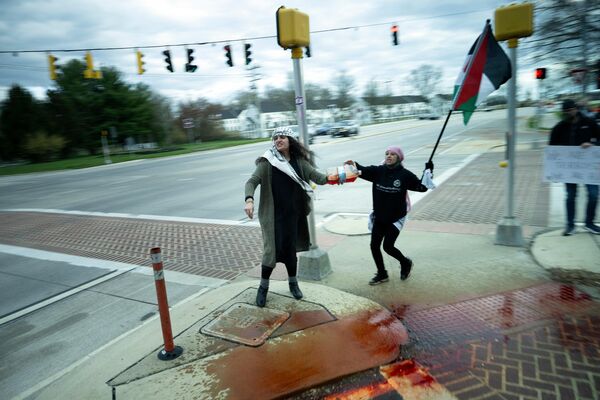 Protesta frente a la caravana del presidente estadounidense en Greenville, Delaware, EEUU. Manifestantes que sostienen una bandera palestina derraman lo que parece un simulacro de sangre al paso del automóvil de Joe Biden, de regreso de la misa del sábado. - Sputnik Mundo