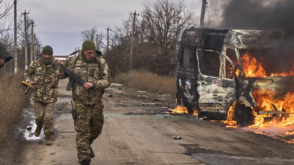Soldados ucranianos pasan junto a un autobús de voluntarios en llamas después de que un dron ruso lo impactara cerca de la ciudad de Artiómovsk  - Sputnik Mundo