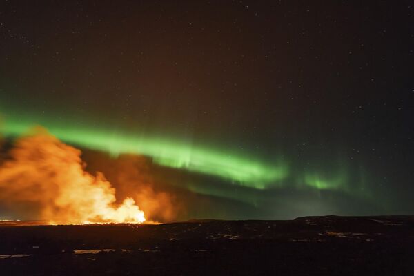 Vista de la zona de erupción con la aurora boreal bailando en el cielo cerca de la ciudad de Grindavík el 28 de marzo de 2024. - Sputnik Mundo