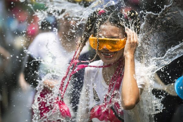 Una mujer se sonríe mientras le salpican con un cubo de agua durante el festival del agua de Songkran, Tailandia. - Sputnik Mundo