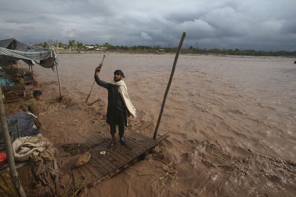 Un hombre se toma una foto en la orilla de un arroyo desbordado tras las fuertes lluvias, en las afueras de Peshawar, Pakistán. - Sputnik Mundo