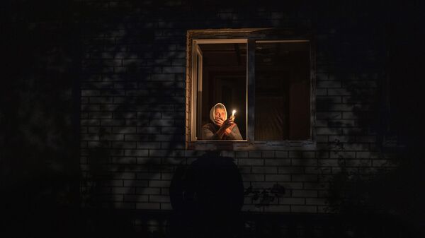 Mujer mira por la ventana mientras sostiene una vela para la luz dentro de su casa durante un corte de energía, en Borodianka, región de Kiev, Ucrania, el 20 de octubre de 2022. - Sputnik Mundo