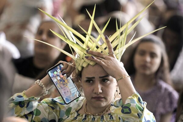 Una mujer cristiana copta ortodoxa ajusta su corona, hecha de hojas de palma, antes de rezar durante una misa de Domingo de Ramos en la capital egipcia de El Cairo. - Sputnik Mundo