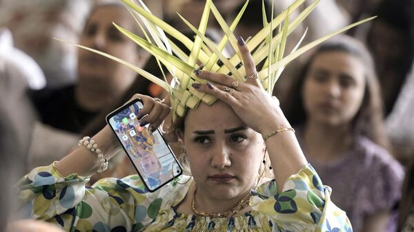 Una mujer cristiana copta ortodoxa ajusta su corona, hecha de hojas de palma, antes de rezar durante una misa de Domingo de Ramos en la capital egipcia de El Cairo. - Sputnik Mundo