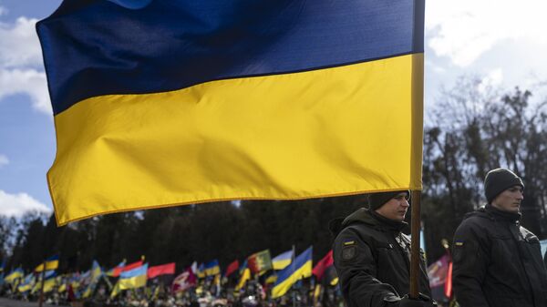Un soldado ucraniano sostiene una bandera ucraniana en un cementerio de Ucrania - Sputnik Mundo