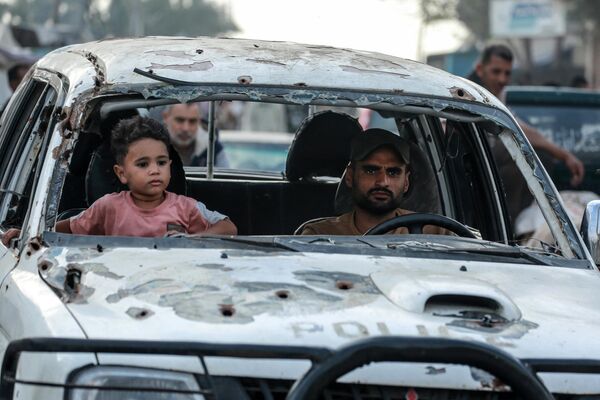 Un niño palestino junto a un hombre conduciendo un automóvil dañado en Deir al Balá, en el centro de la Franja de Gaza. - Sputnik Mundo