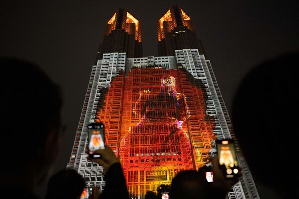 Un grupo de personas toma fotografías del edificio del Gobierno de Tokio, iluminado con un mapping titulado Godzilla: Ataque a Tokio que muestra un Godzilla de 100 metros de altura a escala real. - Sputnik Mundo