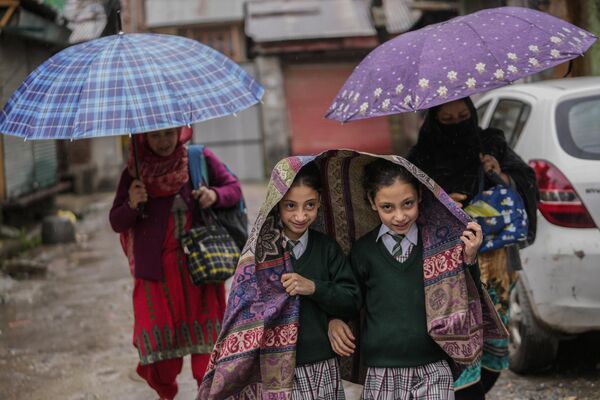 Escolares que regresan a sus casas se cubren la cabeza con un chal de lana mientras llueve en Srinagar, la región disputada de Cachemira, controlada por la India. - Sputnik Mundo