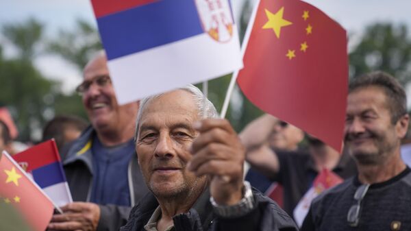Un hombre ondea banderas chinas y serbias mientras espera la llegada del presidente chino Xi Jinping y su homólogo serbio Aleksandar Vucic a las puertas del Parlamento de Serbia. - Sputnik Mundo