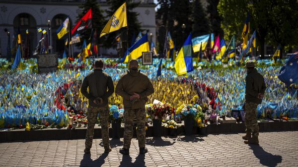 Militares ucranianos junto a banderas ucranianas y fotografías colocadas en memoria de los soldados muertos, en la plaza de la Independencia, en el centro de Kiev, el 20 de abril de 2024  - Sputnik Mundo