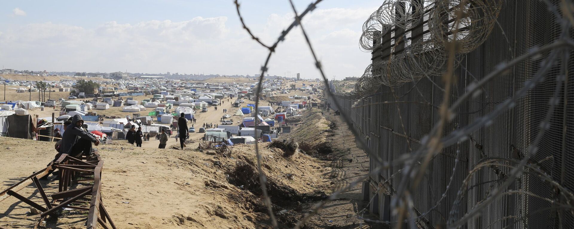 Palestinos desplazados por la ofensiva aérea y terrestre israelí sobre la Franja de Gaza sentados junto a la valla fronteriza con Egipto en Rafah, el 24 de junio, 2024 - Sputnik Mundo, 1920, 16.05.2024