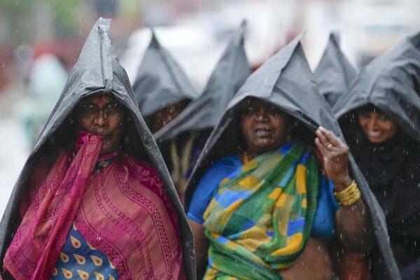 Un grupo de mujeres cubriéndose con impermeables de plástico al verse sorprendidas por un chaparrón repentino en la ciudad de Hyderabad, la India. - Sputnik Mundo