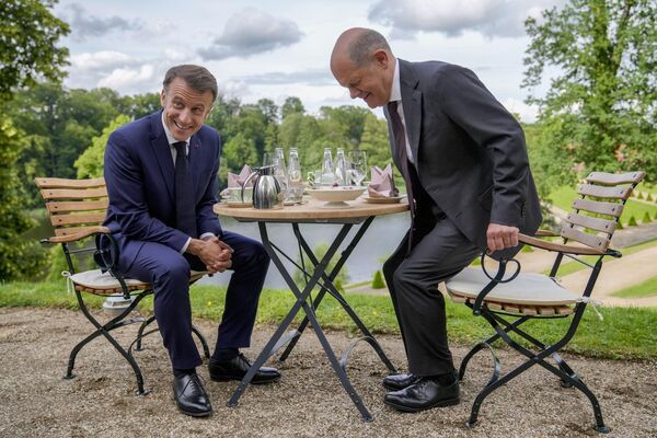 El canciller alemán, Olaf Scholz, y el presidente francés, Emmanuel Macron, se sientan en una mesa en el jardín de la casa de huéspedes del Gobierno alemán en Meseberg, al norte de Berlín. - Sputnik Mundo