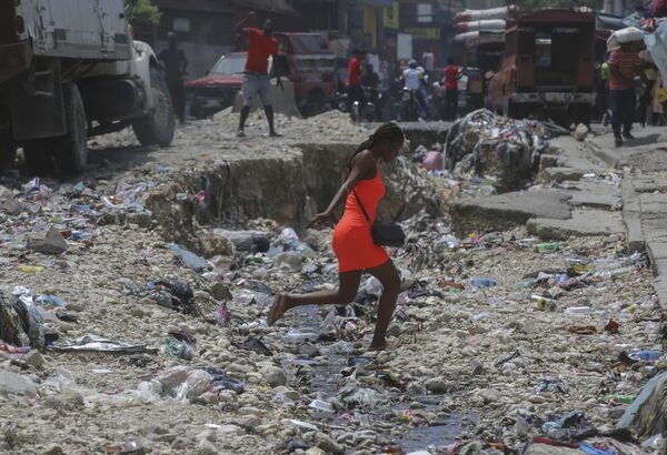Una mujer cruza una alcantarilla llena de basura en Puerto Príncipe, Haití. - Sputnik Mundo