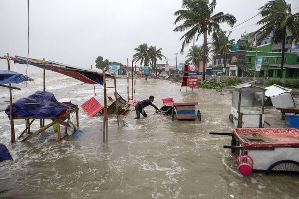 Un hombre rescata un carro y otros materiales mientras el agua fluye hacia la playa de Kuakata, en la costa de la Bahía de Bengala, a causa del ciclón Remal en Barisal, Bangladesh. - Sputnik Mundo
