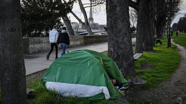 Un indigente duerme en su tienda mientras los peatones caminan cerca del río Sena con la Torre Eiffel al fondo en el centro de París - Sputnik Mundo