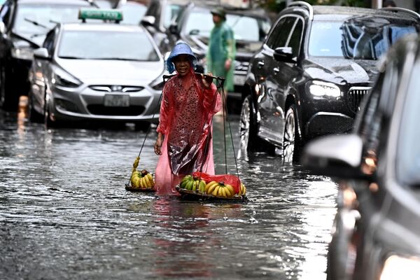 Un vendedor de plátanos vadea una calle inundada en Hanói, Vietnam.  - Sputnik Mundo