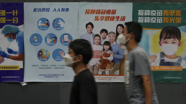 Residentes con mascarillas caminan junto a una pared que muestra varios carteles que animan a la gente a vacunarse contra el COVID-19 a lo largo de una calle de Pekín, China  - Sputnik Mundo