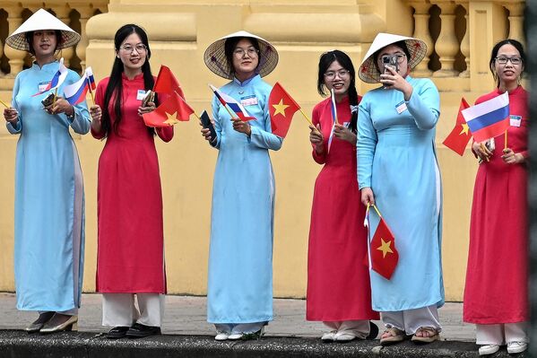 Mujeres con vestidos tradicionales vietnamitas Ao Dai ondean banderas nacionales vietnamita y rusa mientras esperan la llegada del presidente de Rusia, Vladímir Putin, frente al Palacio Presidencial de Hanói el 20 de junio de 2024. - Sputnik Mundo