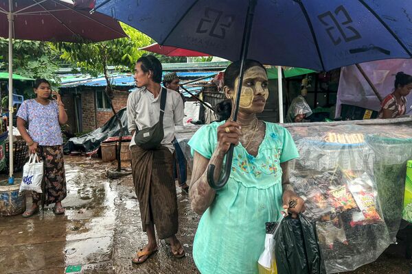 Personas con paraguas esperan en una parada de autobús mientras llueve en la ciudad de Rangún, Birmania. - Sputnik Mundo