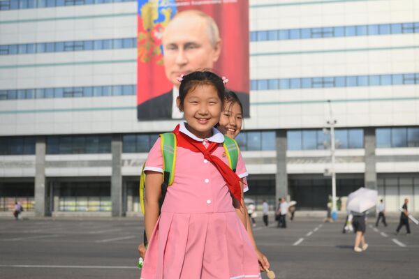 Escolares cerca de un edificio en el que se exhibe una pancarta con un retrato del jefe de Estado ruso, Vladímir Putin, en Pionyang, Corea del Norte. - Sputnik Mundo