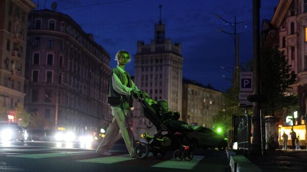 Una mujer empuja un carrito con su hijo a través de una calle oscura, después de que el ayuntamiento cortara las luces de la ciudad para conservar energía en Ucrania, el 14 de abril de 2024  - Sputnik Mundo