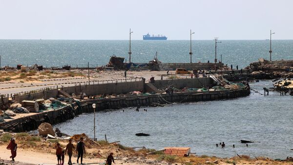 Palestinos caminan junto a un embarcadero en la ciudad de Gaza con vistas a los buques de la Armada frente a la costa como parte de un corredor marítimo humanitario anunciado por el Mando Central de Estados Unidos (CENTCOM) en mayo de 2024.  - Sputnik Mundo