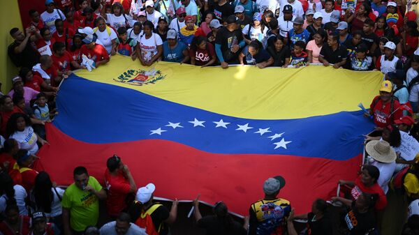 Una bandera venezolana sostenida entre simpatizantes del presidente y candidato presidencial de Venezuela, Nicolás Maduro - Sputnik Mundo