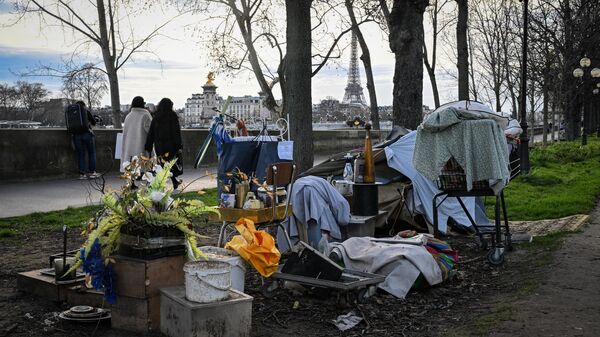 Peatones pasan al lado de un campamento de personas sin hogar cerca del río Sena con la Torre Eiffel al fondo, en el centro de París (Foto de Miguel MEDINA / AFP)
 - Sputnik Mundo