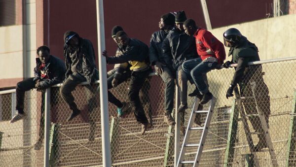 African migrants sit at the top of a border fence, as a Spanish Civil Guard tries to convince them to descend the stairs, during an attempt to cross into Spanish territories, between Morocco and Spain's north African enclave of Melilla December 30, 2014. - Sputnik Mundo