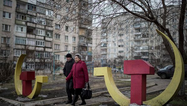 Local residents walk past Soviet-era hammer and sickle sculptures outside an apartment building damaged after Saturday's shellingin Mariupol, Ukraine - Sputnik Mundo
