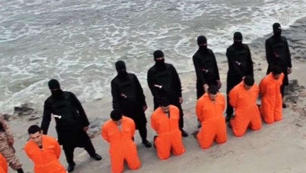 Men in orange jumpsuits purported to be Egyptian Christians held captive by the Islamic State (IS) kneel in front of armed men along a beach said to be near Tripoli, in this still image from an undated video made available on social media on February 15, 2015. - Sputnik Mundo