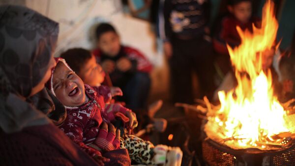 Members of a Palestinian family warm themselves by a fire at the remains of their house that witnesses said was destroyed by Israeli shelling during a 50-day war - Sputnik Mundo