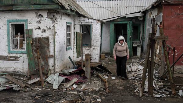 Mujer cuesta cerca de la casa destruida durante los bombardeos en Donbás - Sputnik Mundo