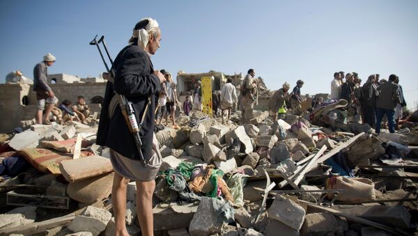 A Houthi Shiite fighter stand guard as people search for survivors under the rubble of houses destroyed by Saudi airstrikes near Sanaa Airport, Yemen - Sputnik Mundo