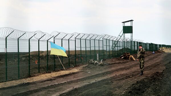 A Ukrainian border guard officer speaks on a phone near a national flag attached to the fence on the Ukrainian-Russian border near Hoptivka, Kharkiv region, eastern Ukraine - Sputnik Mundo