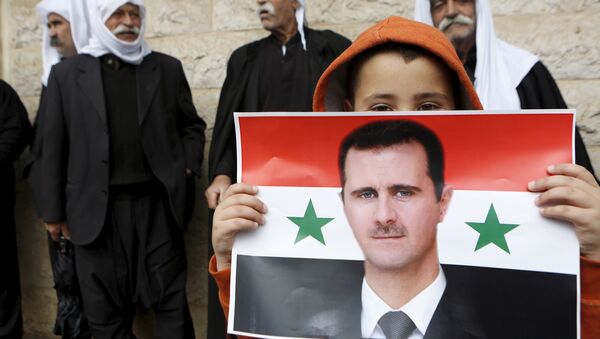 Un niño con la bandera de Siria con la foto de Bashar Asad en sus manos - Sputnik Mundo