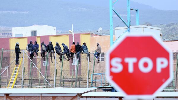Would-be immigrants sit atop a border fence separating Morocco from the north African Spanish enclave of Melilla in the first attempt to jump in on February 19, 2015 - Sputnik Mundo