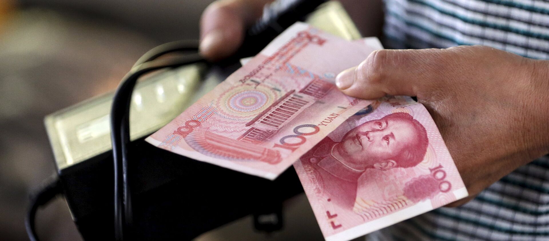 A customer holds a 100 Yuan note at a market in Beijing, August 12, 2015 - Sputnik Mundo, 1920, 22.11.2020