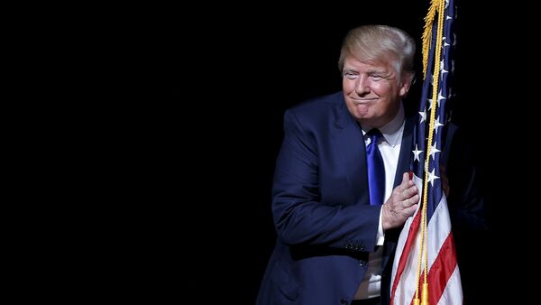 U.S. Republican presidential candidate Donald Trump hugs a U.S. flag - Sputnik Mundo