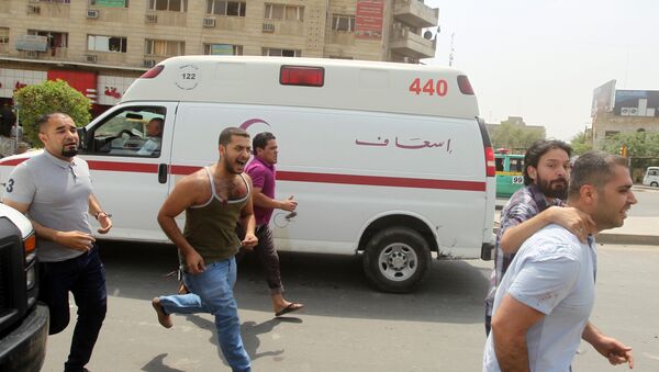 Iraqi men run past an ambulance as an injured man is taken away from the scene of a car bomb blast - Sputnik Mundo