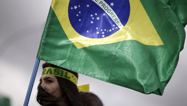 Una manifestante lleva la bandera nacional brasileña durante una protesta - Sputnik Mundo