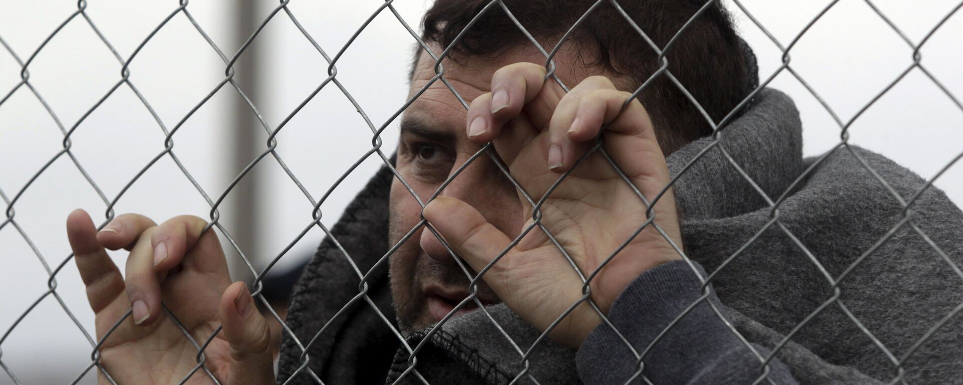 A refugee covered with a blanket looks through a fence as he and other stranded refugees wait for the border crossing to reopen near the Greek village of Idomeni, February 28, 2016. - Sputnik Mundo, 1920, 17.03.2022