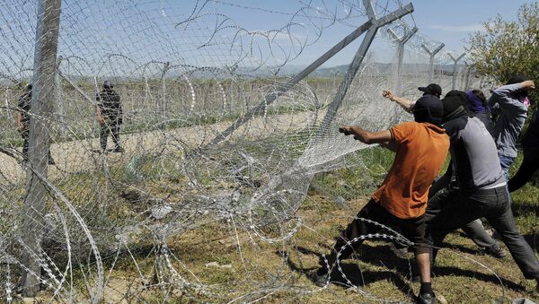 Migrants try to bring down part of a border fence as Macedonian police stand guard at a makeshift camp for refugees and migrants at the Greek-Macedonian border near the village of Idomeni - Sputnik Mundo