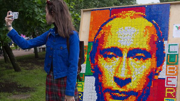 A girl takes a selfie against a portrait of Russian President Vladimir Putin composed of Rubik's Cubes at the festival of the social network VKontakte in St. Petersburg - Sputnik Mundo